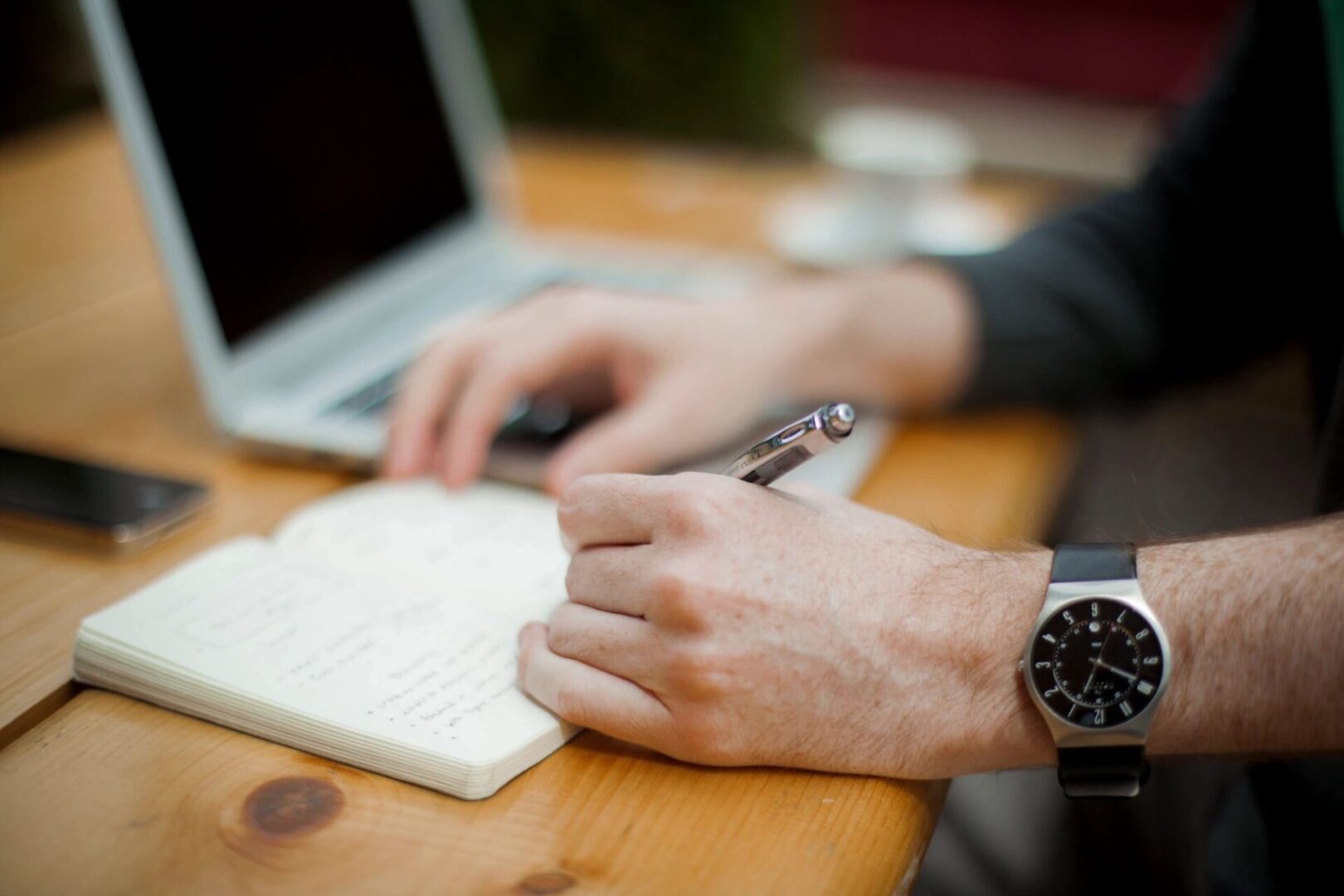 A person writing on paper with a laptop